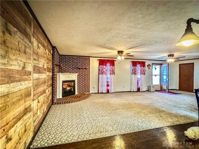 unfurnished living room featuring ceiling fan, wooden walls, a textured ceiling, and a brick fireplace