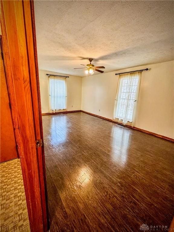 empty room with a textured ceiling, ceiling fan, dark wood-type flooring, and a wealth of natural light