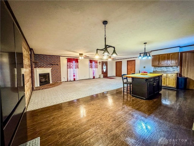 kitchen with ceiling fan, a textured ceiling, a fireplace, decorative light fixtures, and a kitchen island