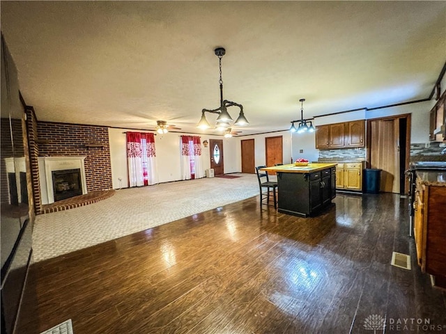 kitchen featuring a center island, hanging light fixtures, a kitchen bar, a fireplace, and ceiling fan with notable chandelier