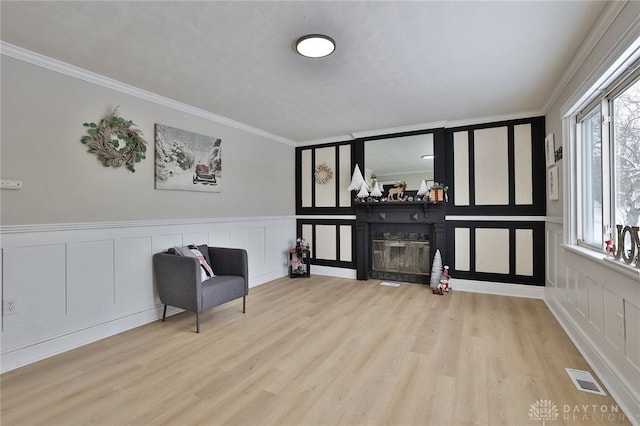 living area with a wealth of natural light, light hardwood / wood-style floors, and ornamental molding