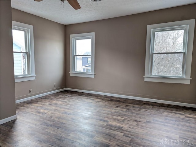 empty room with ceiling fan, a healthy amount of sunlight, and dark wood-type flooring