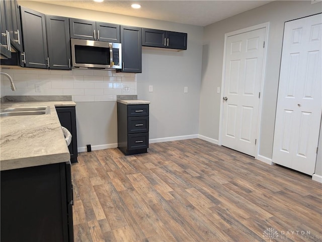 kitchen with backsplash, light stone countertops, wood-type flooring, and sink