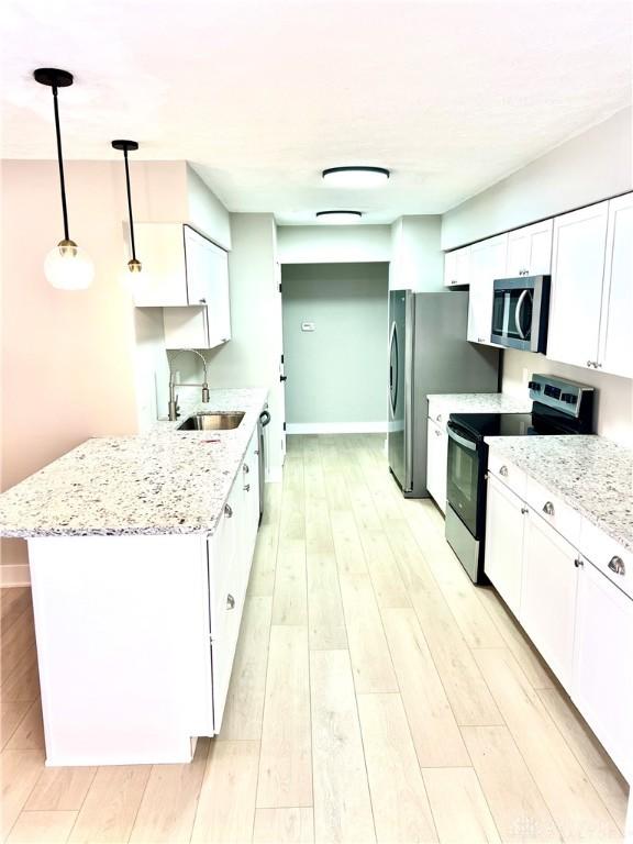 kitchen with stainless steel appliances, sink, light hardwood / wood-style flooring, white cabinetry, and hanging light fixtures