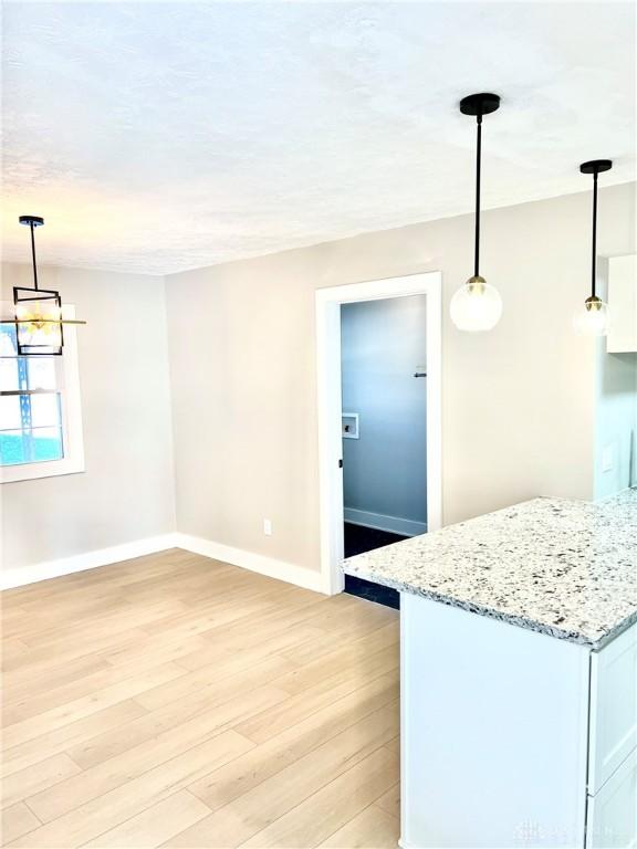 kitchen with white cabinetry, light hardwood / wood-style flooring, light stone countertops, and decorative light fixtures