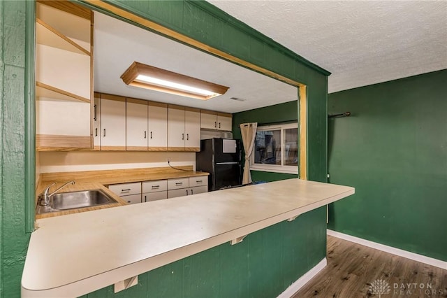 kitchen featuring kitchen peninsula, dark hardwood / wood-style flooring, black fridge, a textured ceiling, and sink