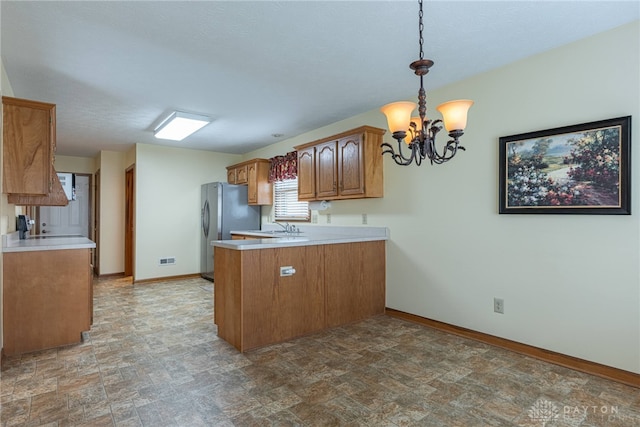 kitchen featuring kitchen peninsula, stainless steel fridge, sink, pendant lighting, and a chandelier