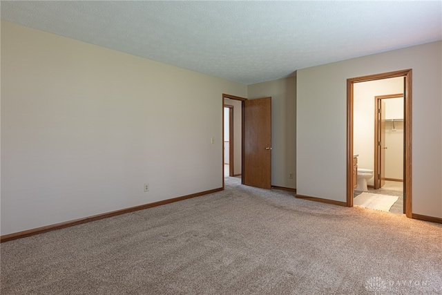 unfurnished bedroom featuring ensuite bath, light colored carpet, a walk in closet, and a closet