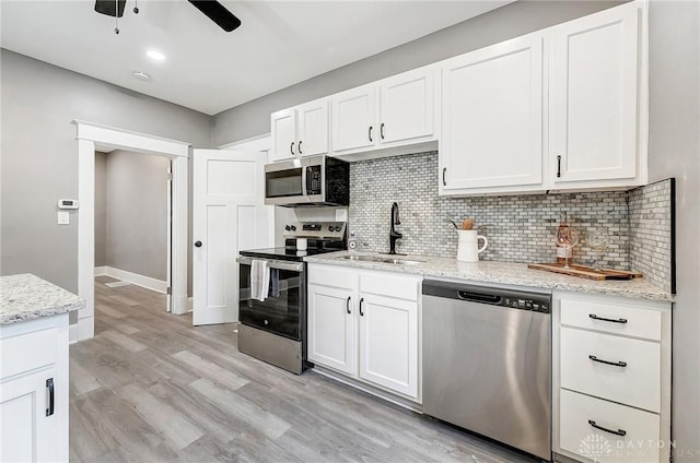 kitchen with light stone countertops, white cabinetry, sink, stainless steel appliances, and decorative backsplash