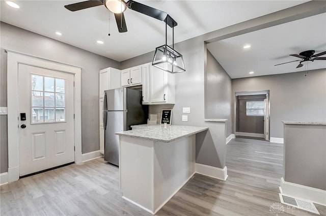 kitchen with white cabinets, stainless steel fridge, kitchen peninsula, and plenty of natural light