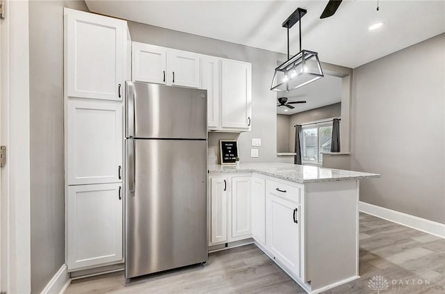 kitchen with stainless steel fridge, light stone countertops, white cabinetry, and kitchen peninsula