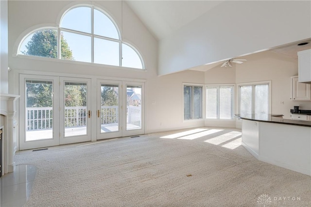 unfurnished living room with a glass covered fireplace, carpet, a wealth of natural light, and high vaulted ceiling