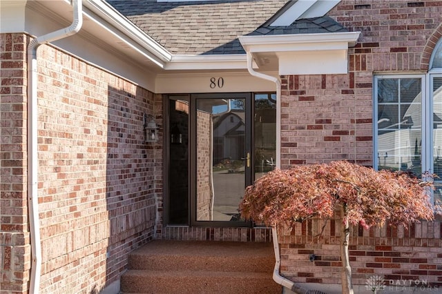 view of exterior entry featuring brick siding and a shingled roof