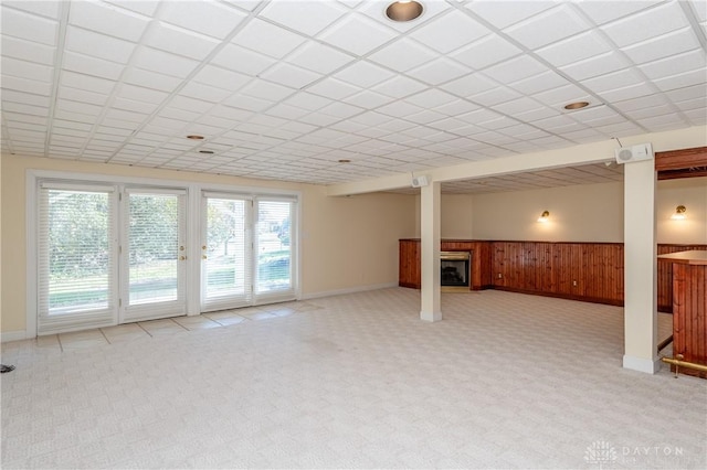 below grade area featuring a paneled ceiling, light carpet, a glass covered fireplace, and wood walls