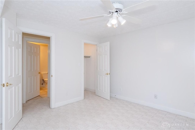 unfurnished bedroom with baseboards, carpet floors, a walk in closet, and a ceiling fan