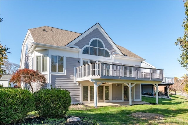 rear view of property featuring a lawn, roof with shingles, a deck, and a patio area