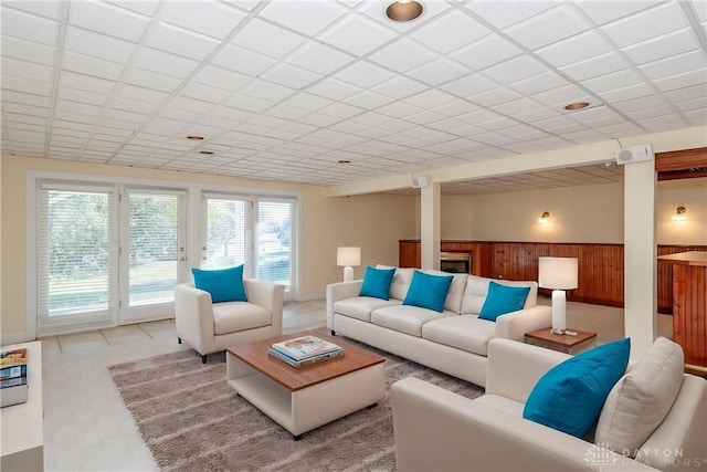 living area featuring a paneled ceiling, wooden walls, and wainscoting