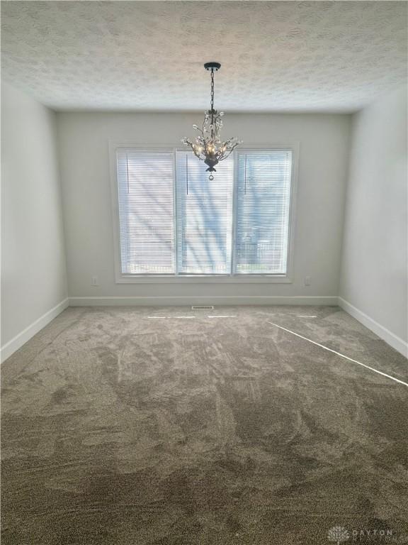 carpeted spare room featuring a wealth of natural light, a notable chandelier, baseboards, and a textured ceiling