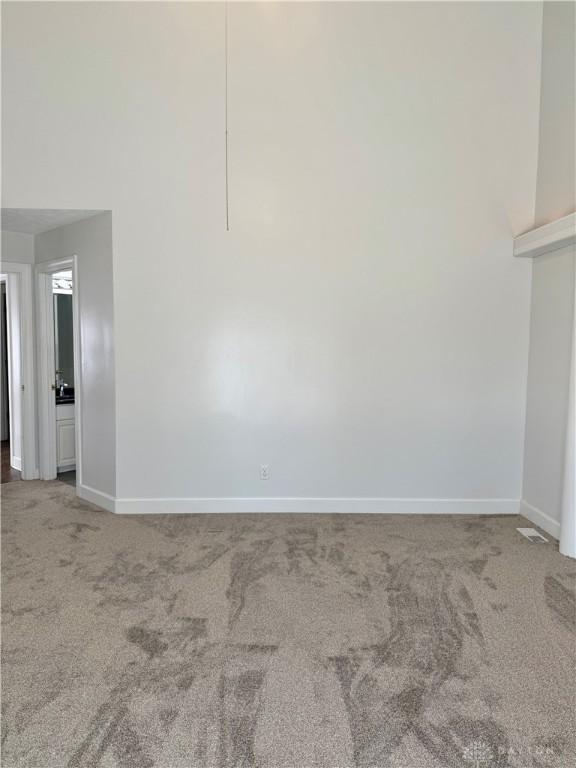 spare room with a towering ceiling, baseboards, and carpet floors