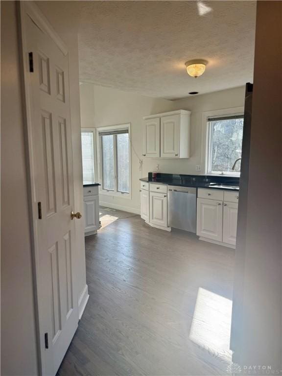 kitchen with dark countertops, dark wood finished floors, dishwasher, white cabinets, and a textured ceiling