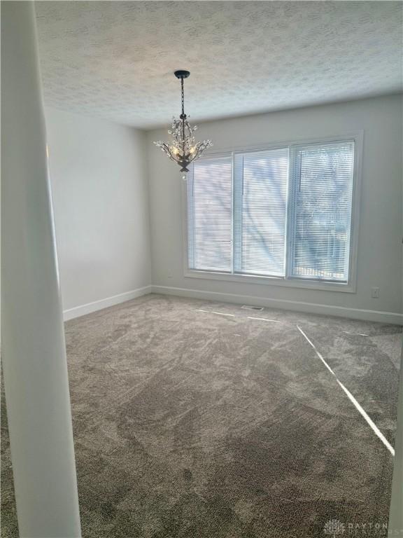 carpeted spare room with a notable chandelier, baseboards, and a textured ceiling