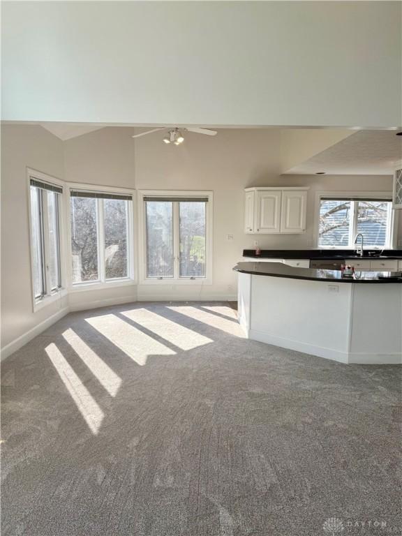 unfurnished living room featuring a wealth of natural light, baseboards, carpet floors, and lofted ceiling