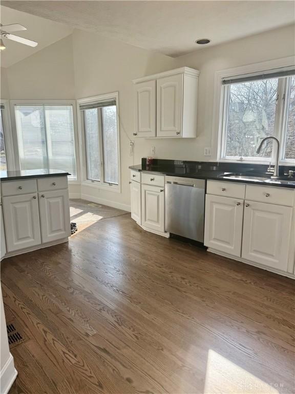 kitchen featuring dark countertops, dishwasher, lofted ceiling, white cabinetry, and a sink