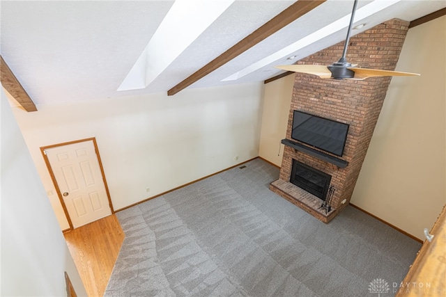 unfurnished living room with ceiling fan, light colored carpet, lofted ceiling with skylight, and a fireplace