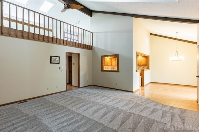 unfurnished living room with beamed ceiling, ceiling fan with notable chandelier, carpet flooring, and high vaulted ceiling