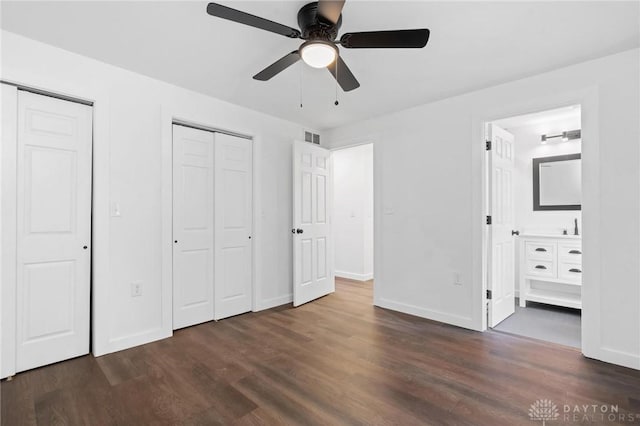 unfurnished bedroom with ensuite bath, ceiling fan, two closets, and dark hardwood / wood-style floors