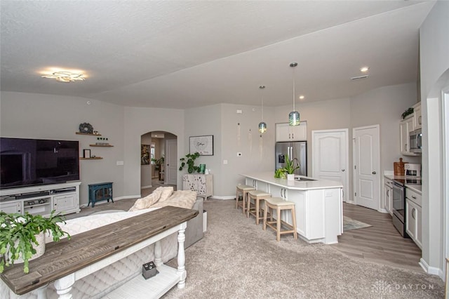 kitchen featuring a center island with sink, a kitchen breakfast bar, hanging light fixtures, appliances with stainless steel finishes, and white cabinetry