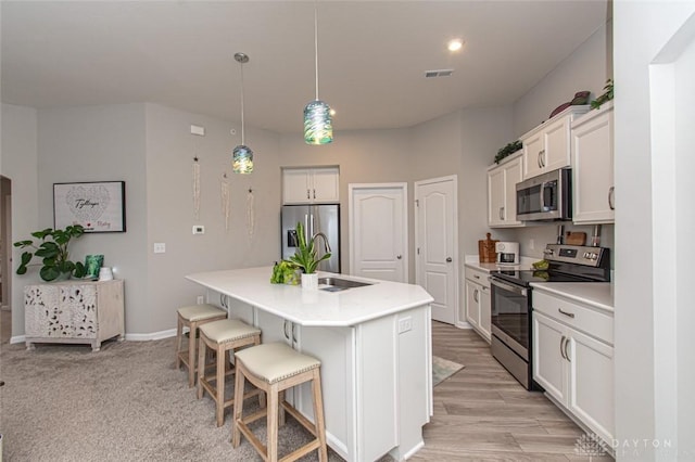 kitchen featuring white cabinetry, sink, stainless steel appliances, an island with sink, and pendant lighting