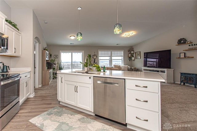 kitchen featuring stainless steel appliances, a kitchen island with sink, sink, white cabinets, and hanging light fixtures