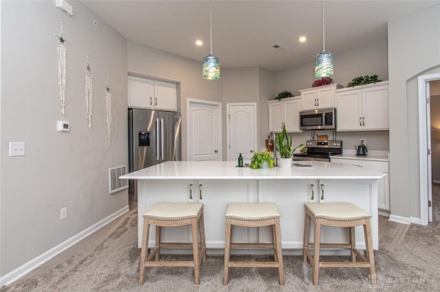 kitchen with appliances with stainless steel finishes, decorative light fixtures, white cabinetry, and a kitchen island with sink