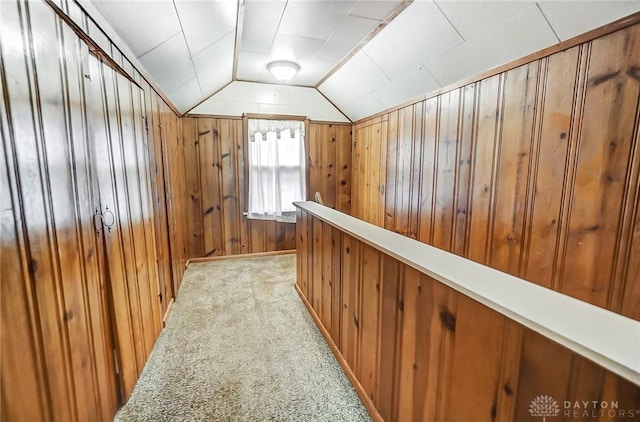 hall with wood walls, light colored carpet, and lofted ceiling