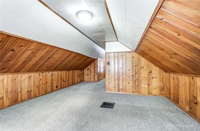 bonus room with wood walls, light carpet, and vaulted ceiling