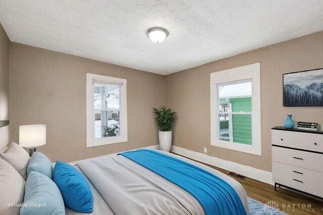 bedroom featuring multiple windows, dark hardwood / wood-style floors, and a textured ceiling