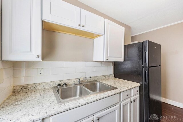 kitchen featuring sink, black fridge, light stone countertops, decorative backsplash, and white cabinets