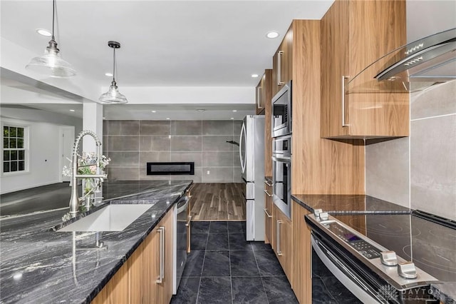 kitchen featuring sink, dark stone counters, decorative light fixtures, tile walls, and appliances with stainless steel finishes