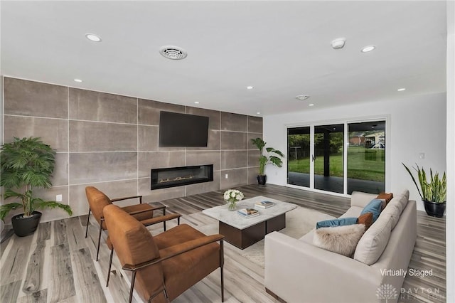 living room with a fireplace, light hardwood / wood-style floors, and tile walls