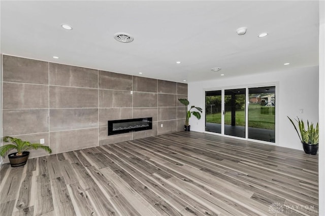 unfurnished living room featuring hardwood / wood-style floors, tile walls, and a tile fireplace