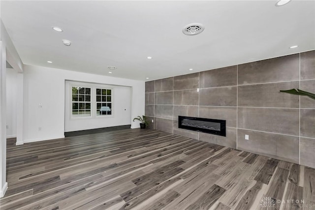 unfurnished living room with wood-type flooring and a tile fireplace