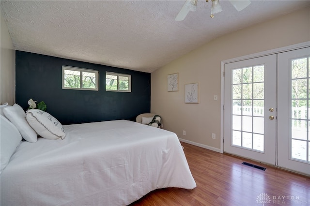 bedroom featuring access to outside, wood finished floors, vaulted ceiling, french doors, and a textured ceiling