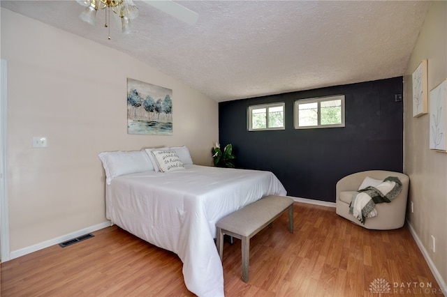 bedroom featuring light wood finished floors, a textured ceiling, vaulted ceiling, baseboards, and a ceiling fan