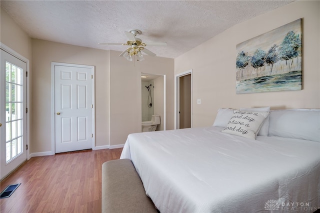 bedroom featuring wood finished floors, a textured ceiling, baseboards, ensuite bathroom, and ceiling fan