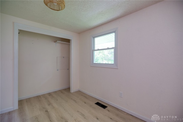 unfurnished bedroom featuring light wood finished floors, a textured ceiling, a closet, and baseboards