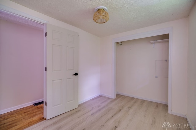 unfurnished bedroom featuring light wood-style flooring, a textured ceiling, baseboards, and a closet