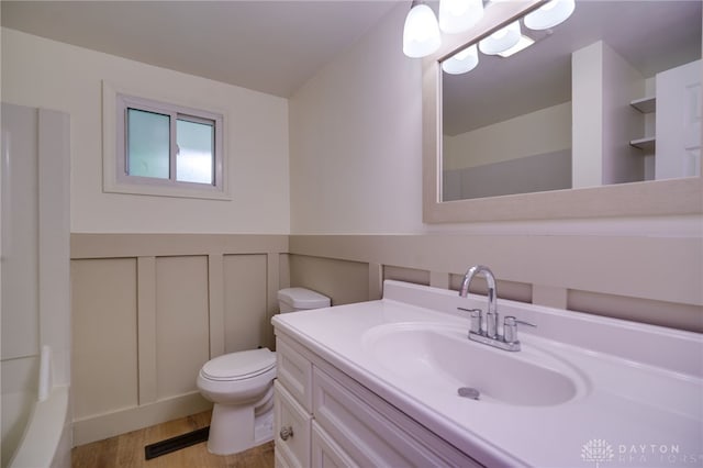 bathroom with wood finished floors, a decorative wall, toilet, vanity, and a wainscoted wall
