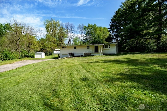 rear view of property featuring driveway, a storage unit, an attached garage, a yard, and an outdoor structure