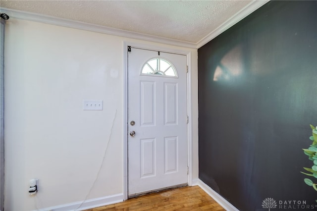 foyer featuring a textured ceiling, ornamental molding, light wood-style floors, and baseboards